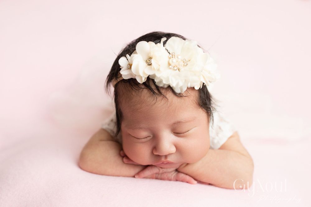 Sleeping newborn on pink background wearing white floral headband.