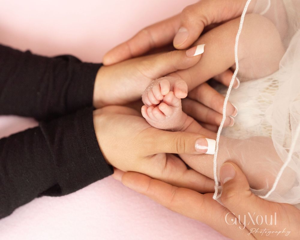 Adult hands tenderly holding tiny newborn fingers on pink background.