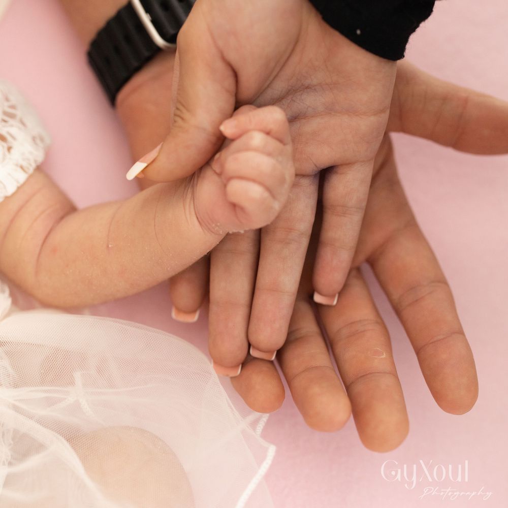 Close-up of adult and baby hands touching against pink fabric background.