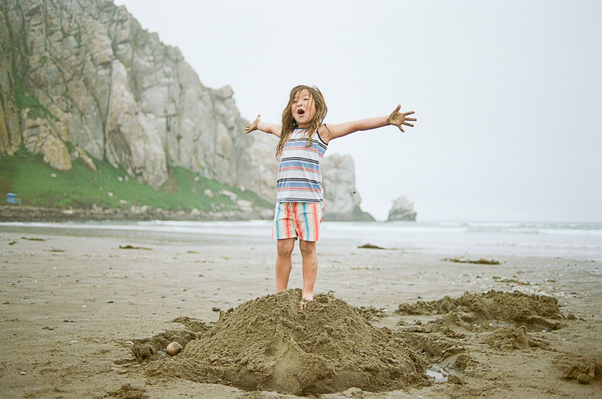 Sandy beach landscape with cliff formations and a figure playing on a large mound of sand.
