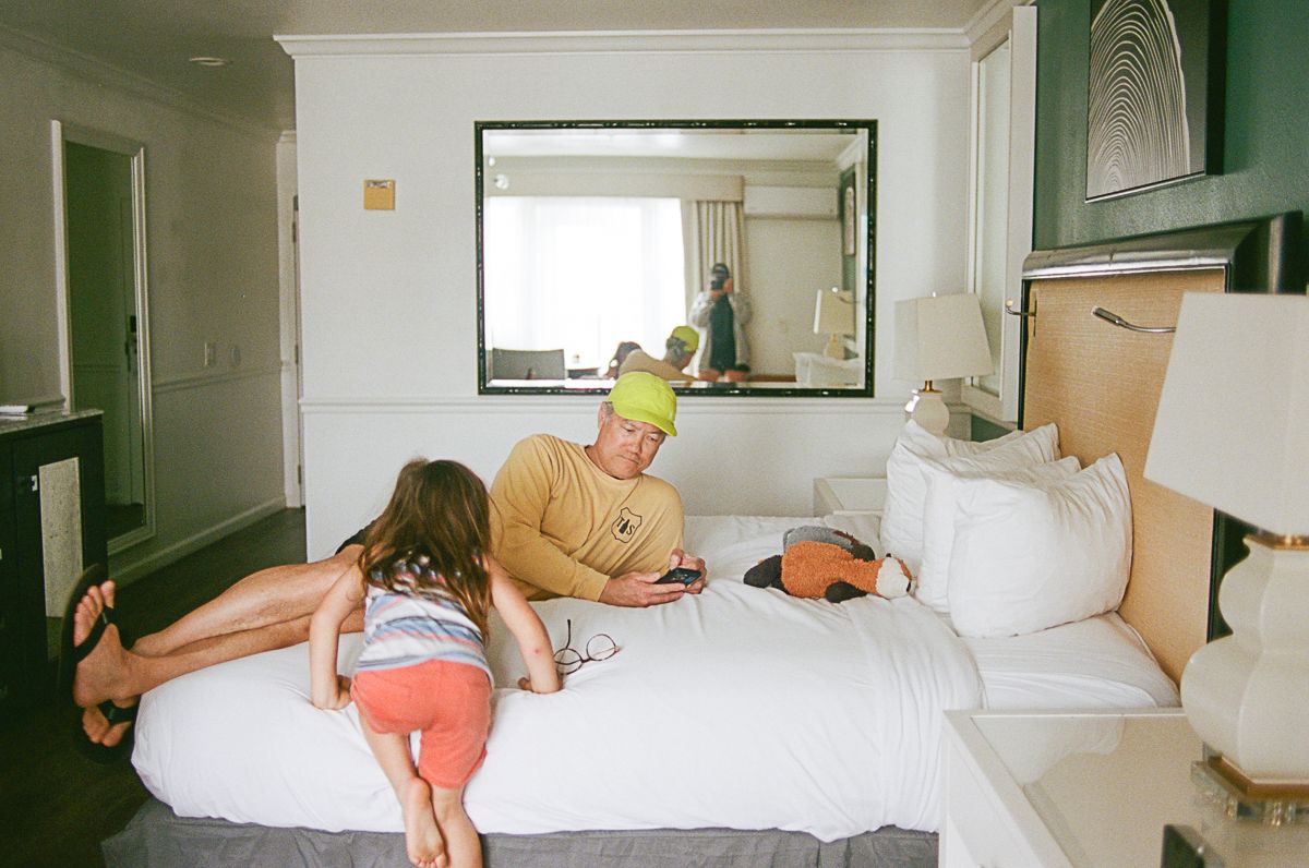 Interior shot of a bright hotel room with people relaxing on a white bed.