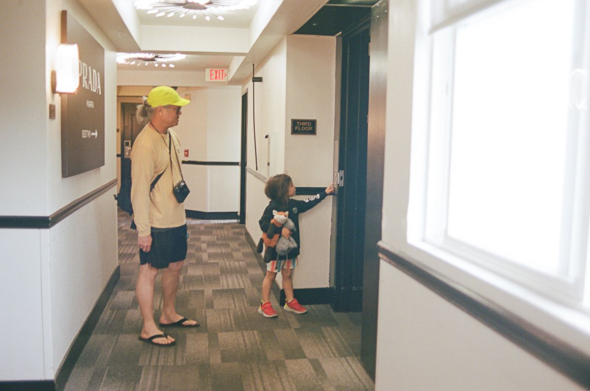 People walking down a carpeted hallway in what appears to be a hotel or apartment building.