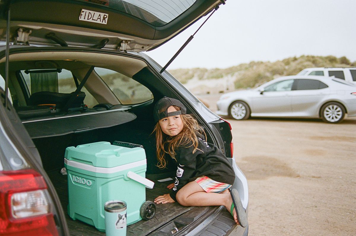 Car trunk open at beach parking lot with camping gear and coolers packed inside.