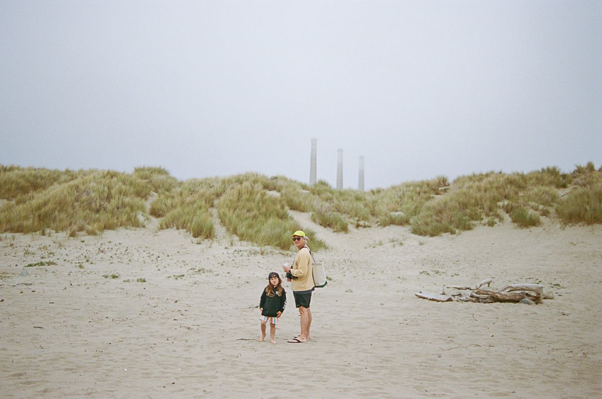 Two figures walking along misty sand dunes on an overcast beach.
