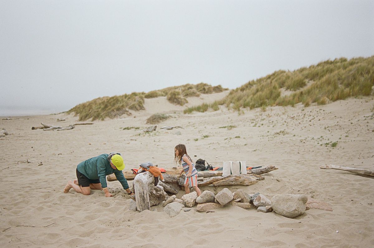 Children playing and lying in the sand on a foggy beach with sand dunes in the background.