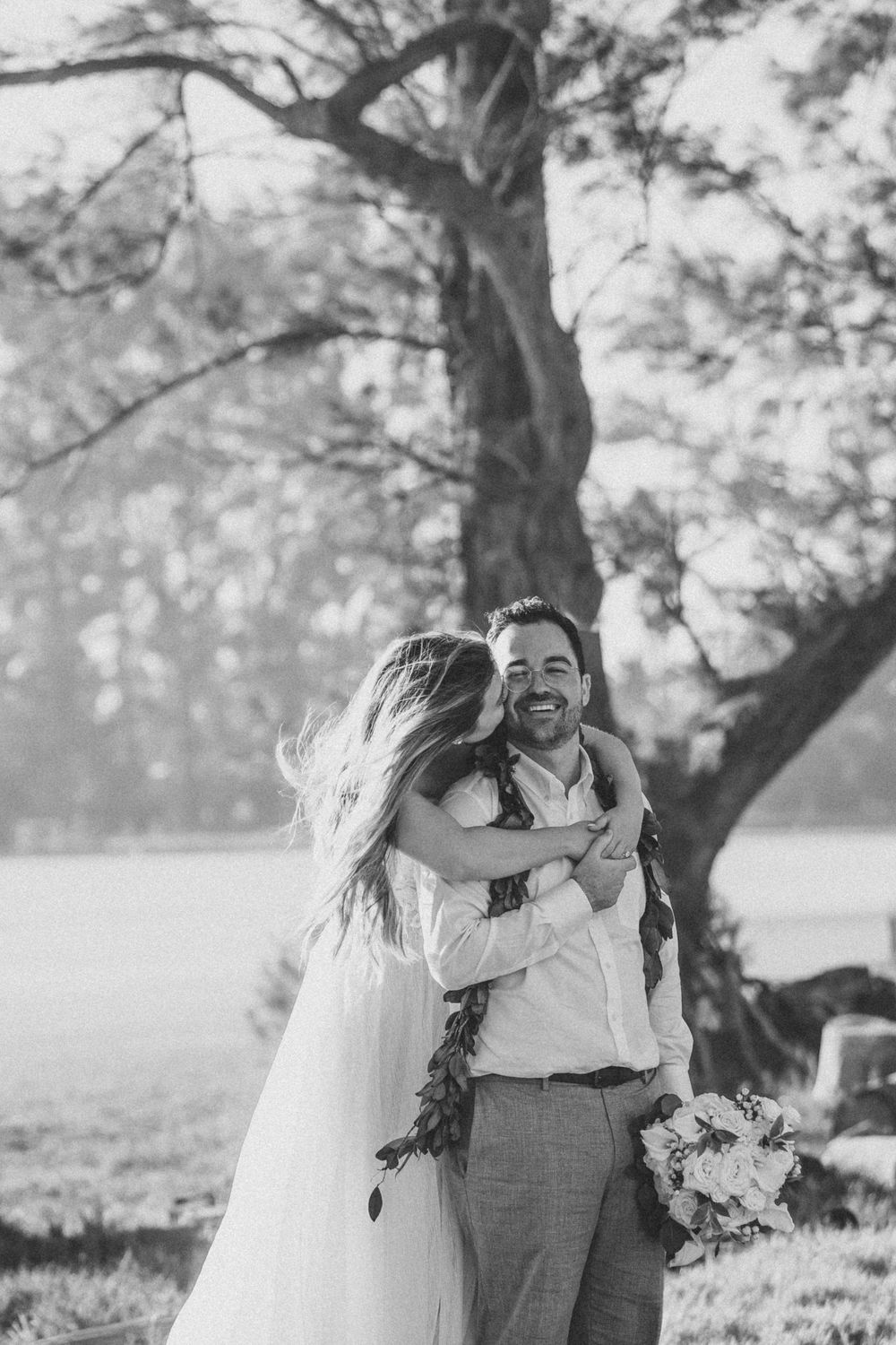 A joyful couple shares intimate moments in a series of black and white outdoor wedding photos under trees.