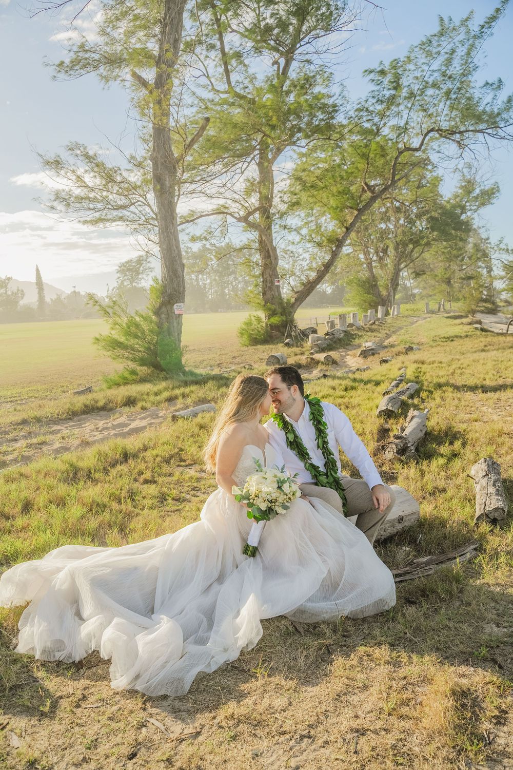 Newlywed couple in wedding attire laying on grassy hillside during golden hour photoshoot.