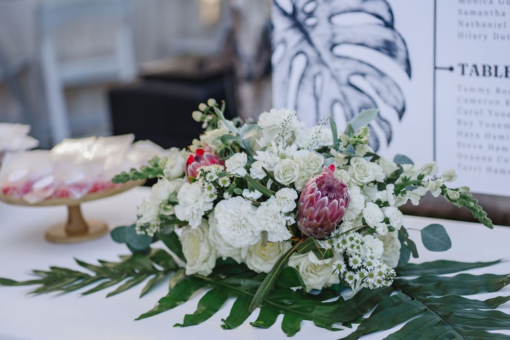 Elegant floral centerpiece with white roses and pink blooms arranged on monstera leaves at a wedding table setting.