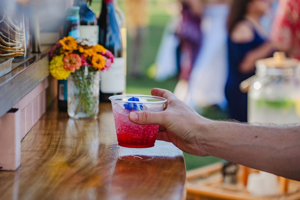 A hand pours a vibrant pink cocktail into a glass with ice at a bar or restaurant.