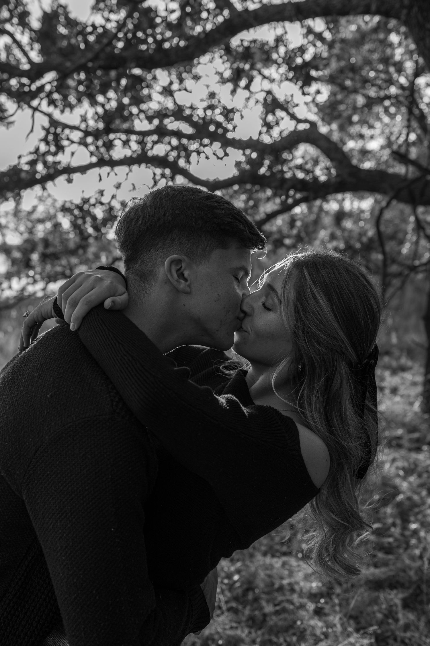 A black and white intimate portrait of a couple sharing a romantic moment outdoors.