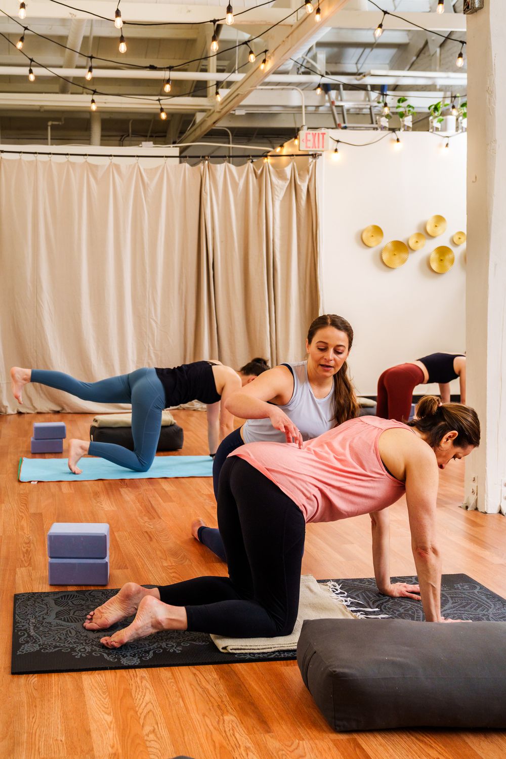 Students practicing yoga poses with blocks in a studio with string lights.