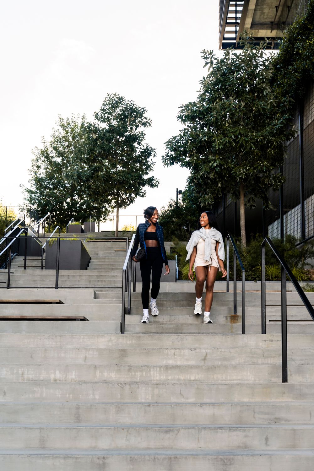 Two people sitting and talking on concrete steps with metal railings in an urban setting during daytime.