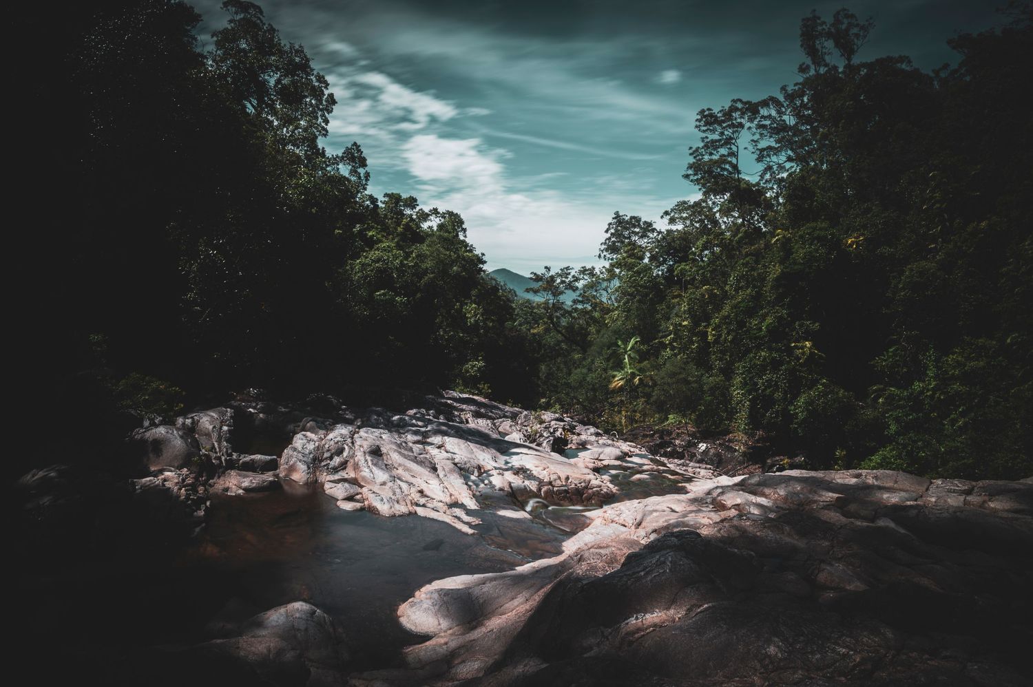 Moody landscape of a rocky creek bed under dramatic teal-colored storm clouds.