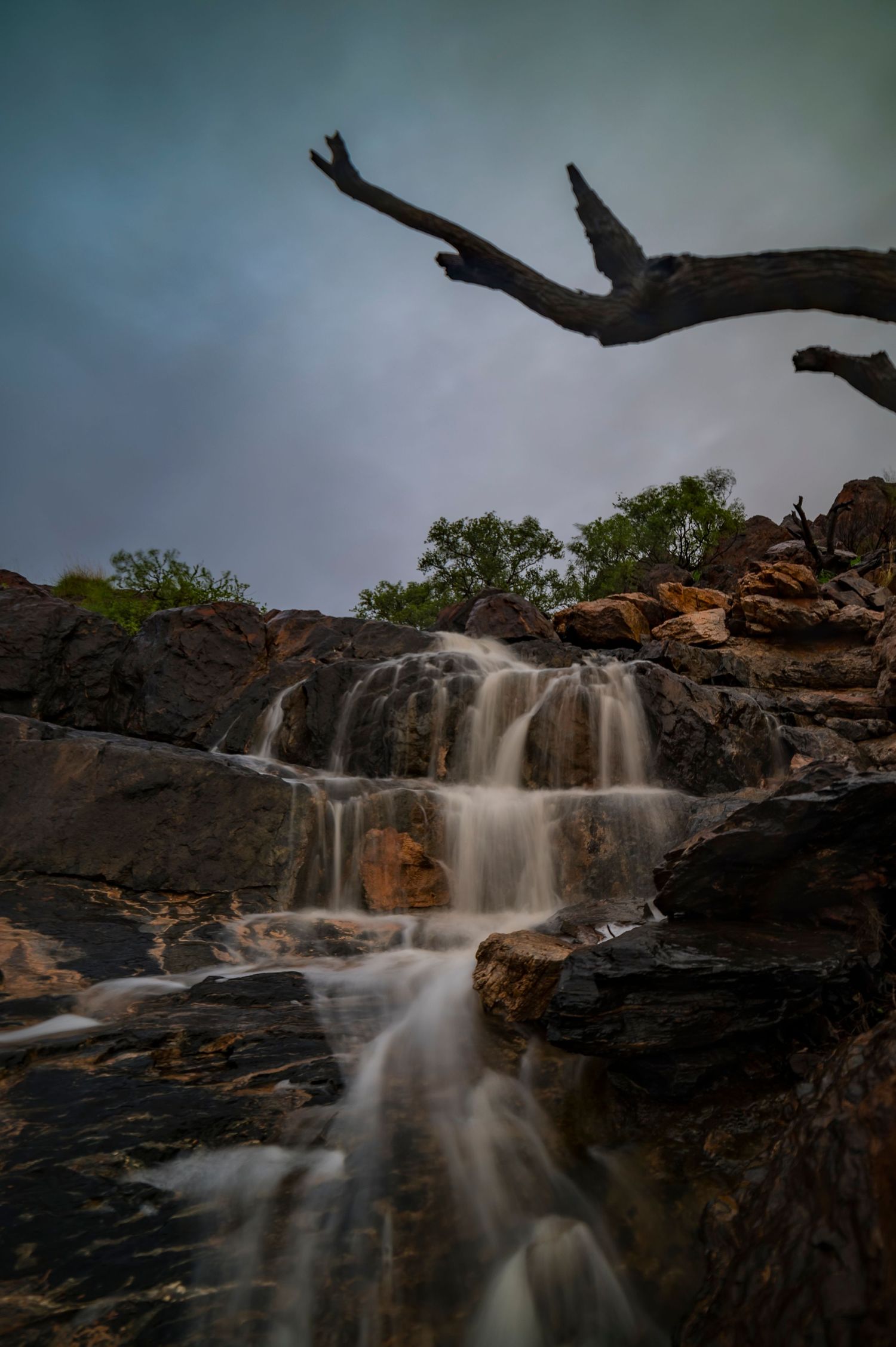 Long exposure waterfall cascading over dark rocky cliffs at dusk with moody storm clouds overhead.