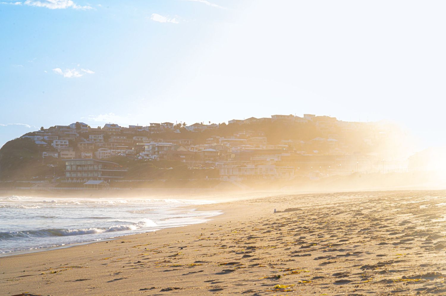 Panoramic view of a sandy beach coastline at golden sunset with waves rolling in.