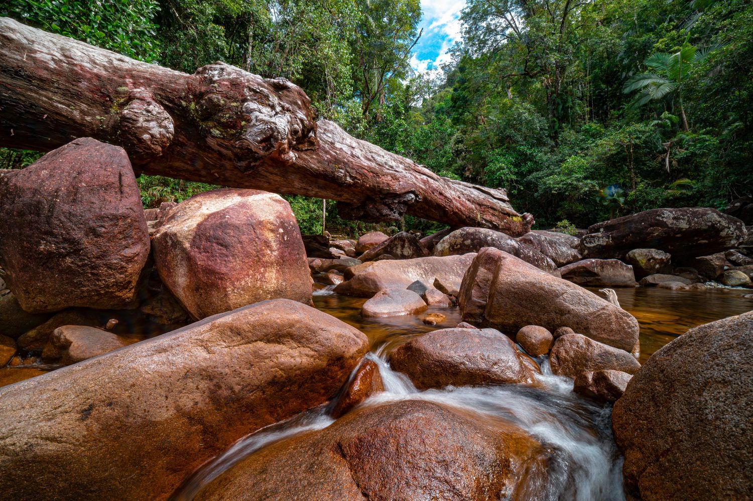 Sunlit waterfall streaming over red rock formations in a tropical forest setting.