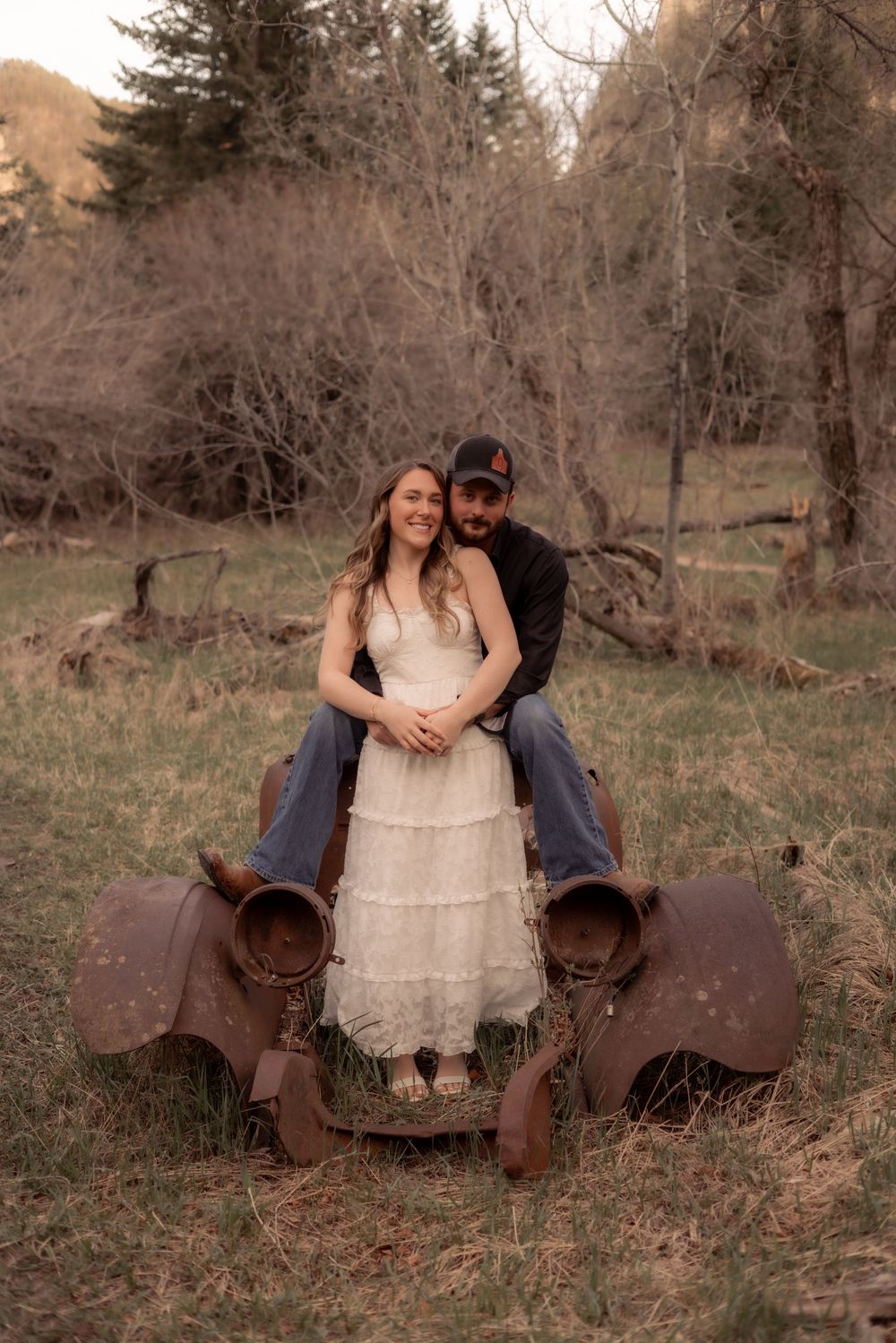 A couple embraces on rustic saddles in a wooded outdoor setting during golden hour.