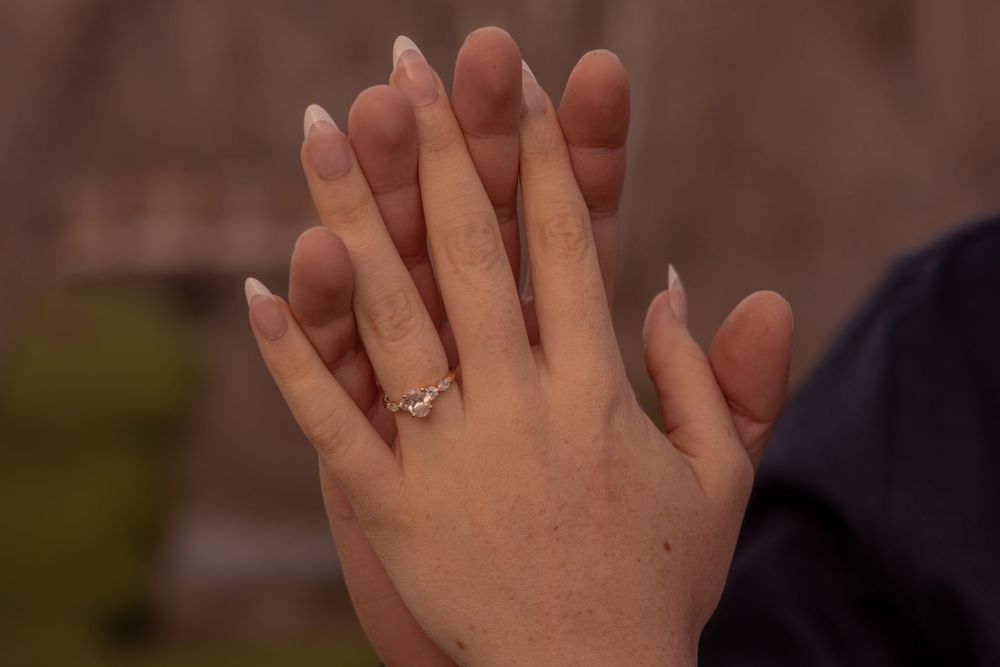 Two hands clasped together showing an engagement ring with a blurred background.