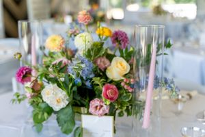 Elegant wedding centerpiece with colorful roses, peonies and delicate blue flowers on white tablecloth.
