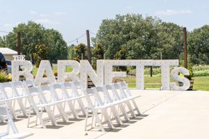 White BARNETTS sign with rows of empty chairs set up for outdoor wedding ceremony.