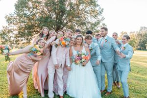 Joyful wedding party in blue and pink attire poses together on a grassy lawn.