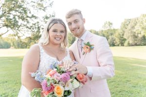 Wedding portrait with couple in light pink and white holding vibrant floral bouquet.