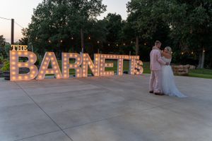 Illuminated marquee letters spelling BARNETT at an outdoor wedding venue at dusk.