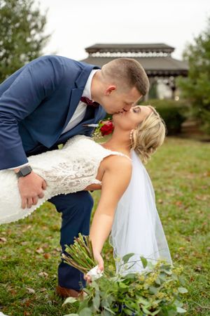 A romantic wedding dip kiss pose outdoors with a gazebo in the background.