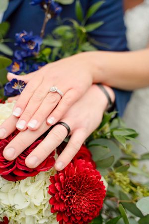 Wedding rings and hands displayed on a bouquet with red and white flowers.