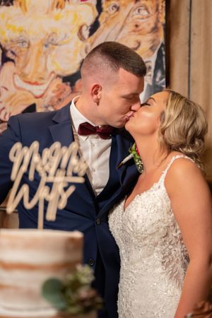 A romantic kiss shared between newlyweds in front of their wedding cake.