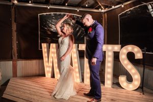 Dancing couple posing in front of illuminated WATTS letters at wedding reception.