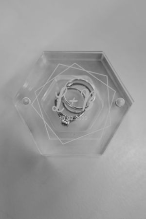 A wedding ring set displayed on a modern hexagonal clear acrylic holder.