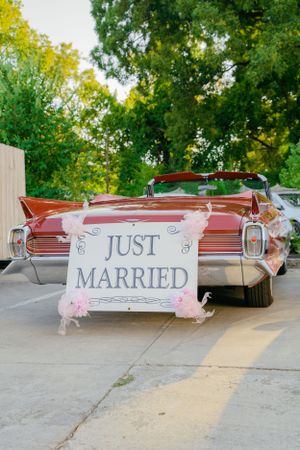 Classic red convertible car with 'Just Married' sign decorated with pink flowers.