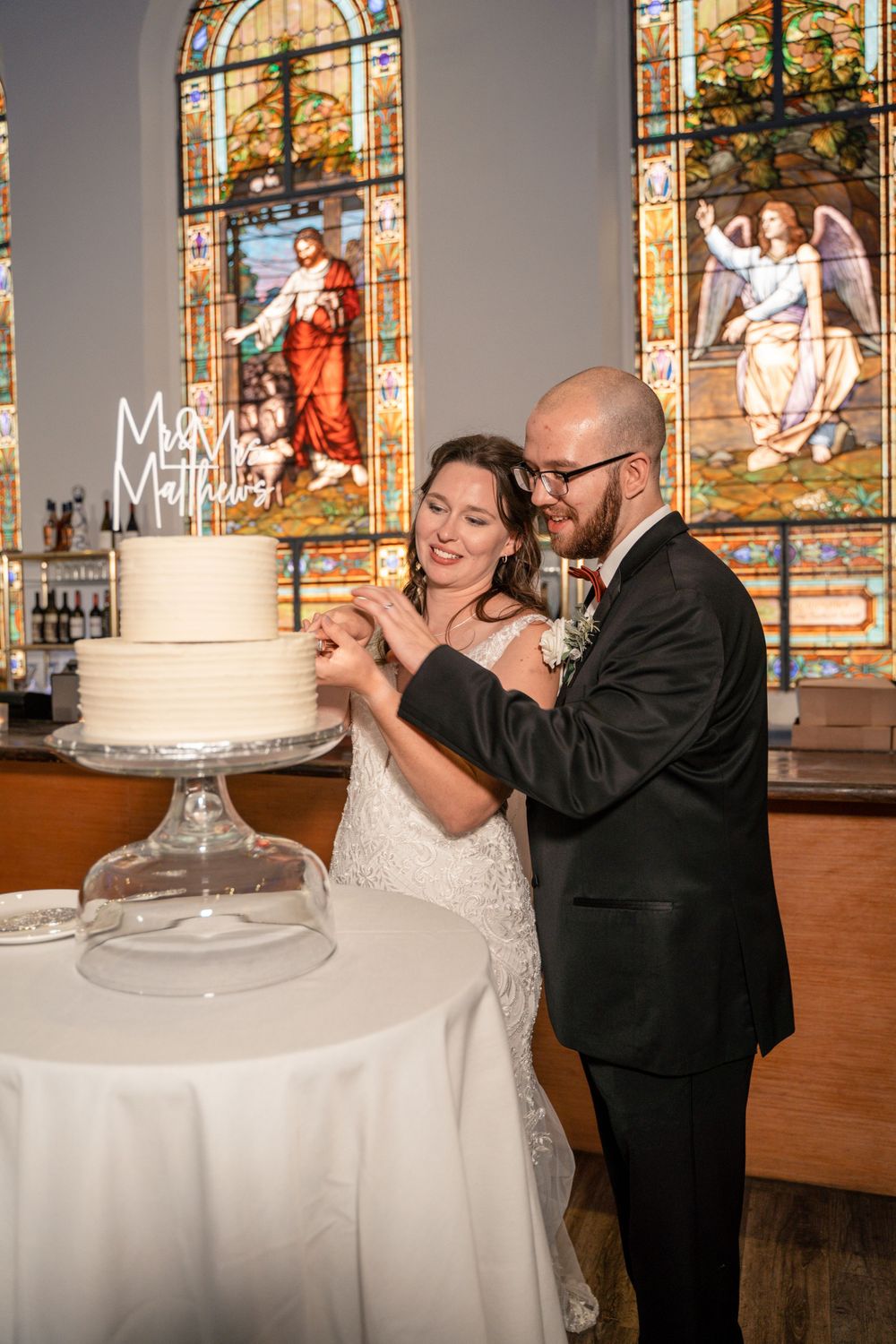 Couple cutting their wedding cake in front of stained glass windows.