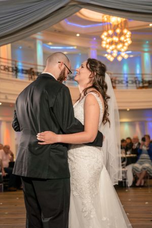 Dancing couple in a ballroom with elegant chandeliers and draped ceiling.