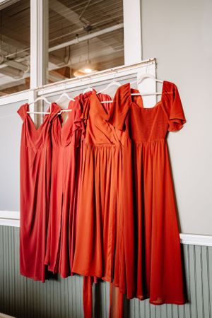 A collection of elegant rust-colored bridesmaid dresses hanging on display against a white wall.
