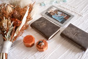 Wedding details flatlay with dried flowers, leather notebooks and decorative orange objects.