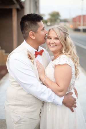 Happy couple in wedding attire embrace on a street corner.