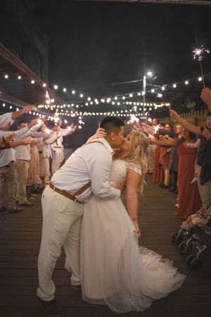 Wedding couple shares romantic kiss during sparkler exit at night.