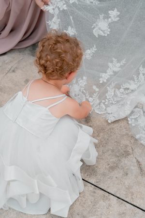 Small child in white dress touching intricate lace details on wedding dress.