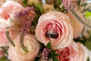 Close-up of wedding rings nestled in a blush pink rose surrounded by floral arrangements.