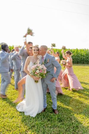 Wedding party celebrating on a sunny day with cornfield in the background.