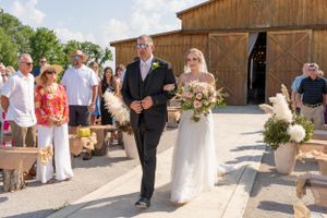 Wedding ceremony processional outside rustic barn venue with floral decorations.