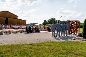 Outdoor wedding ceremony setup with guests seated and wedding party standing at rustic venue.