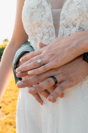 Close-up of wedding rings and lace dress details in golden sunlight.