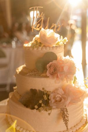 Three-tiered white wedding cake decorated with delicate pink roses and a gold topper.