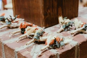 Wedding boutonnieres with coral flowers and greenery arranged on wooden steps.