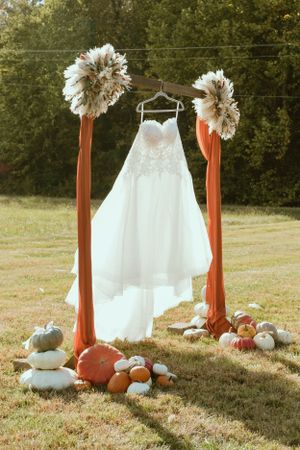 White wedding dress hanging between orange poles with pumpkins and floral decor.