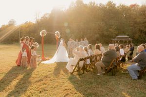 Outdoor sunset wedding ceremony with guests seated on lawn chairs.