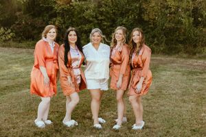A group wearing matching coral-colored satin robes and white sneakers pose together on grass.